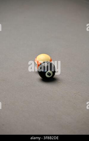 Commercial close-up photograph of the black 8-ball positioned closely in front of another striped billiard ball on a gray pool table felt, capturing the texture and game details. Stock Photo