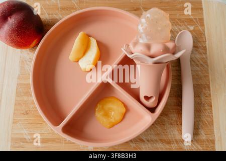 Aesthetic infant feeding accessories set with fruit puree and teether nibbler on a wood surface. Perfect stock photo for eco-friendly baby products Stock Photo