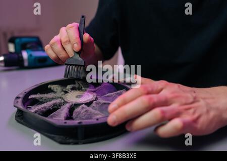 Close-up of hands using small brush to clean thick dust from computer cooling fan. Concept for PC maintenance, repair service, DIY hardware upgrade Stock Photo