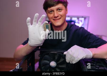 Smiling man wearing white protective gloves holding up central processing unit, demonstrating computer hardware for technology and maintenance concept Stock Photo