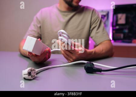 Mans hands holding white multi outlet power strip and bundled cable near plugs and computer tower, illustrating electronics setup, cable management Stock Photo