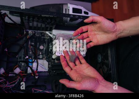Close-up of male hands holding clump of dust removed from computer heatsink. Technician performing PC maintenance to prevent overheating. Moody lighti Stock Photo