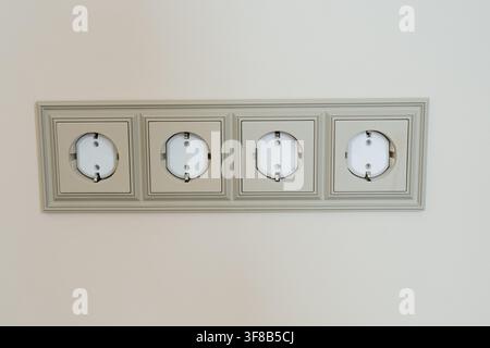 Horizontal frame with four European ground electric power outlets mounted on a beige wall. Perfect for electrical installation, home automation, power Stock Photo