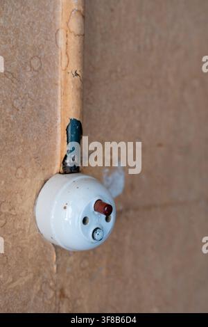 Close-up of an old vintage ceramic electrical switch and socket mounted on a stained textured wall with peeling paint on the wire tube. Stock Photo