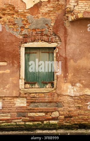 View of a weathered brick wall with a green wooden shuttered window in Venice, Veneto, Italy. Stock Photo