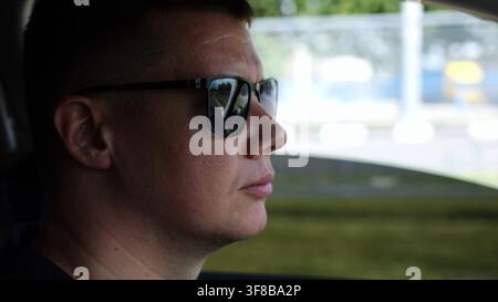 Profile of confident man driving a motor car at town. Male face of male driver in sunglasses looking concentrated to urban road while riding Stock Photo