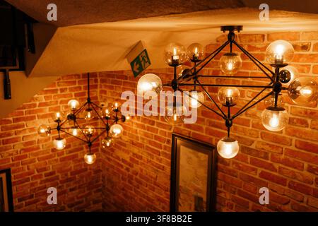 Stylish geometric pendant lights glowing above a wooden staircase with brick wall. Perfect stock image for modern cafe interiors, industrial style Stock Photo