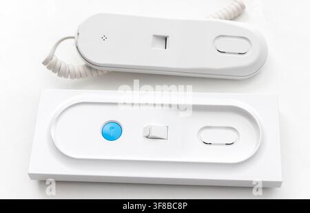A modern white intercom handset lies near its wall mount unit Stock Photo