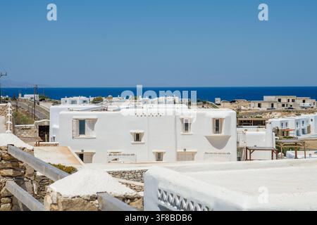 View of white-washed Cycladic architecture with flat roofs and stone walls overlooking the blue Aegean Sea in Mykonos, Greece. Stock Photo