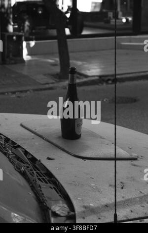Black and white street reflection shot showing a bottle on a table viewed through a shop window with urban surroundings reflected. Stock Photo