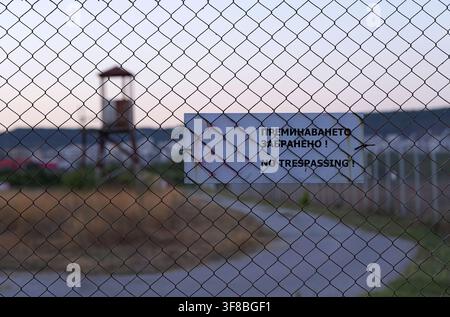 Chain link fence in focus with a no trespassing sign written in english and bulgarian. Standing in front of a blurred background showing a distant wat Stock Photo