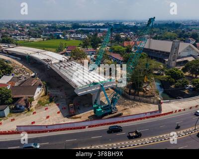 Aerial view of bridge construction site with large crawler cranes, workers on the girder concrete deck, and surrounding urban landscape in Special Reg Stock Photo