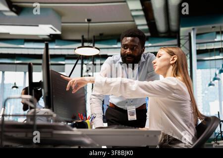 Helpful coworker mentoring young employee in startup office, reviewing code scripts on PC. African american tech company team leader guiding intern doing software development Stock Photo