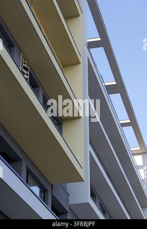 Modern residential building facade featuring multiple projecting balconies and strong architectural lines creating a pattern against a clear blue sky Stock Photo