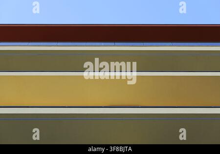 Modern building facade featuring horizontal lines and color blocks, creating an abstract and minimalist design under a clear blue sky Stock Photo