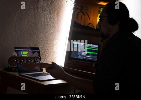 A musician focuses on producing music late at night from a home recording setup. Stock Photo