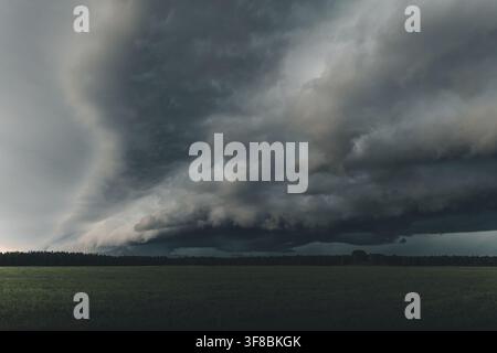 View of a dramatic shelf cloud forming over a green field and forest line in Saxby, Laane County, Estonia. Stock Photo