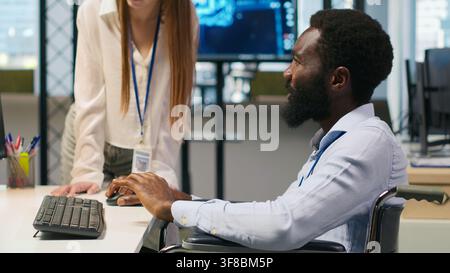 Junior dev and coworker in wheelchair developing software applications, optimizing code. Female technician and colleague with paraplegia in office using AI to solve bottlenecks, camera A Stock Photo