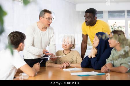 Positive man discussing volunteer project with associates at table Stock Photo