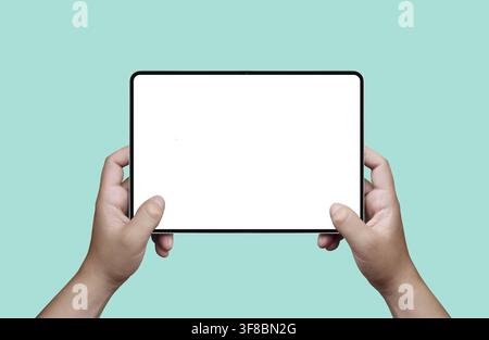 Hands holding a digital tablet with blank white screen mockup on a pastel mint background Stock Photo