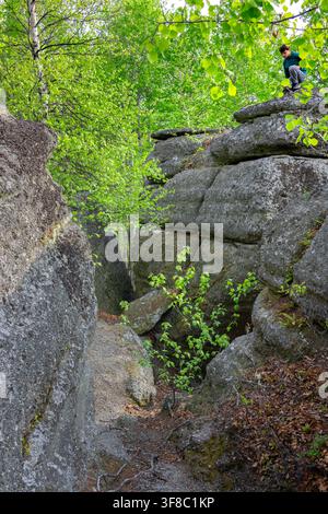 Teenager hiker is standing on the top of rock structures geological site, prehistoric ocean trench now in a green forested environment. Rim rocks, Wes Stock Photo