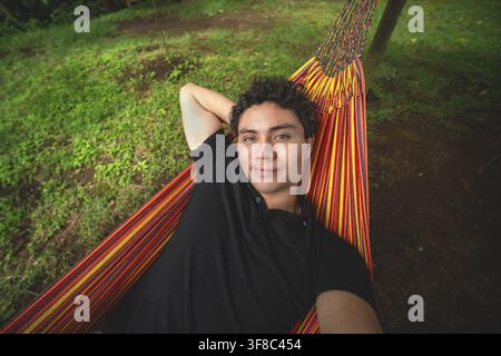 Smiling man taking a selfie while lying in a hammock. Attractive man smile resting in a hammock in nature Stock Photo