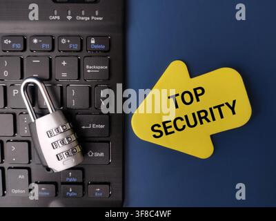 A combination padlock rests on a black laptop keyboard beside a yellow arrow sign reading TOP SECURITY. Stock Photo
