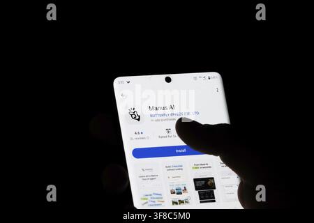 Hand holding smartphone with Manus AI app download page highlighted in a dark scene Stock Photo