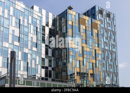 Exterior view of a modern building featuring a unique colorful facade with pixelated glass and metal panels in blue, white, and yellow tones. Stock Photo