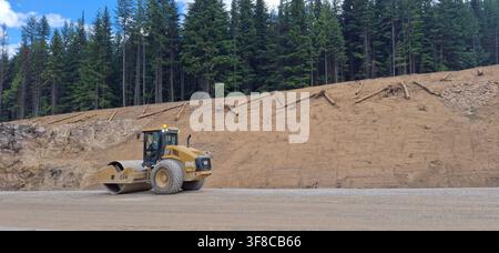 TRANS-CANADA HIGHWAY, CANADA - 10 JULY 2026: A heavy-duty yellow CAT soil compactor vehicle operating on a gravel roadbed during a highway expansion p Stock Photo
