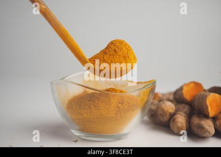 Turmeric powder is shown with fresh turmeric roots nearby Stock Photo
