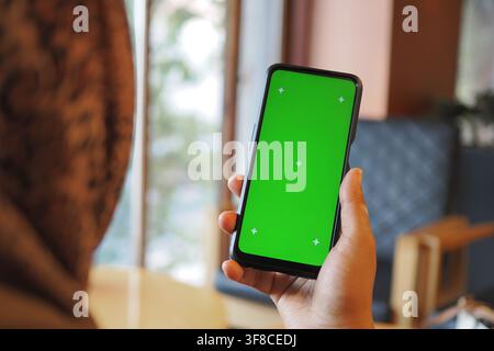 Hand holding smartphone with green screen indoors Stock Photo