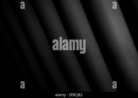 Sleek macro photography of a black textured surface featuring a precise geometric grid pattern. The material is arranged in elegant wavy folds with hi Stock Photo