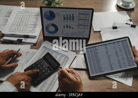 Business people meeting financial documents with calculator, and laptop charts on a desk, comparing figures and discussing data analysis for reporting Stock Photo