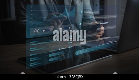 Person uses a large language model assistant on a smartphone beside a laptop, interacting with chatbot panels and analytics dashboard to support AI as Stock Photo