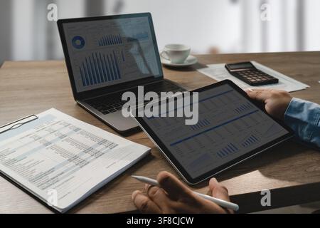 Tablet and laptop display financial dashboards beside printed reports and a calculator, showing data analysis and planning workflow for accounting rev Stock Photo
