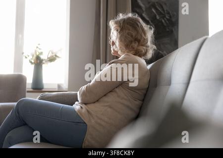 Peaceful senior woman sitting by window looking outside thoughtfully Stock Photo