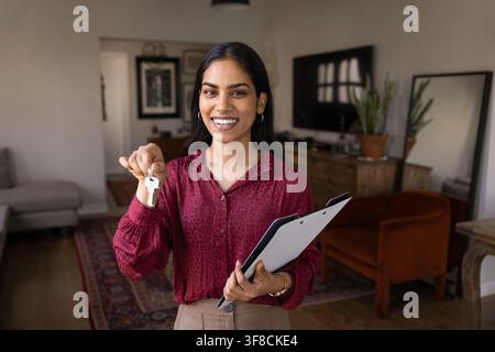 Smiling realtor woman holding house keys and clipboard Stock Photo