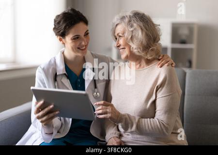 Female doctor consulting senior patient at home using digital tablet Stock Photo