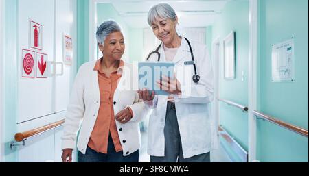 Doctor, checkup and woman at hospital with tablet, test results and medical history for diagnosis. Mature people, walking or consulting in lobby with Stock Photo