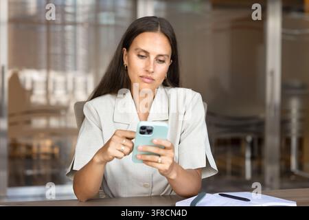 Adult Caucasian businesswoman checking messages on smartphone in office Stock Photo