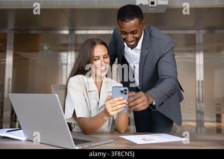 Multiethnic smiling team members watching online content on smartphone Stock Photo