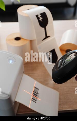 Barcode scanner reading a shipping label beside a label printer and paper rolls for marketplace orders. Packaging automation streamlines barcode Stock Photo