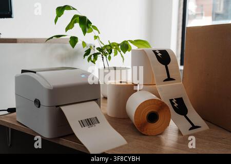 Label printer, paper rolls and fragile shipping labels for small business order fulfillment. Packaging automation streamlines ecommerce operations and Stock Photo
