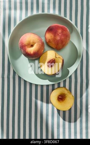 Fresh ripe peaches illuminated by warm sunlight on a blue striped tablecloth, creating a bright and summery fruit background with a natural outdoor at Stock Photo