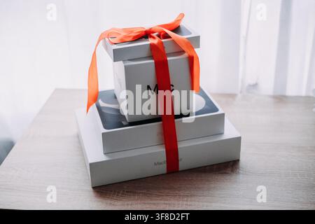 Stack of Apple boxes tied with red ribbon bow on wooden table. Apple bundle gift wrapped, mac ipad macbook gift set, entire apple ecosystem gifted Stock Photo