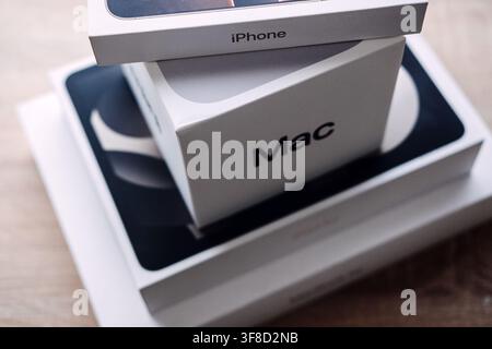Mac box with Apple logo sits on stacked iPad and MacBook boxes on wooden table. Apple product stack mac ipad, mac mini ipad air macbook, apple Stock Photo