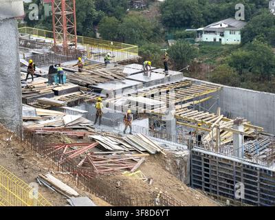 View of construction workers in safety gear working on a concrete foundation with rebar and wooden planks at a hillside building site in Sariyer, Ista Stock Photo