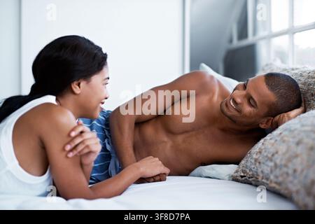 Couple, relax and holding hands on bed with smile, love and discussion on calm morning. Happy, people and laying down at house with conversation Stock Photo