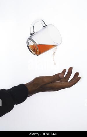 surreal floating glass cup pouring tea above open hand Stock Photo